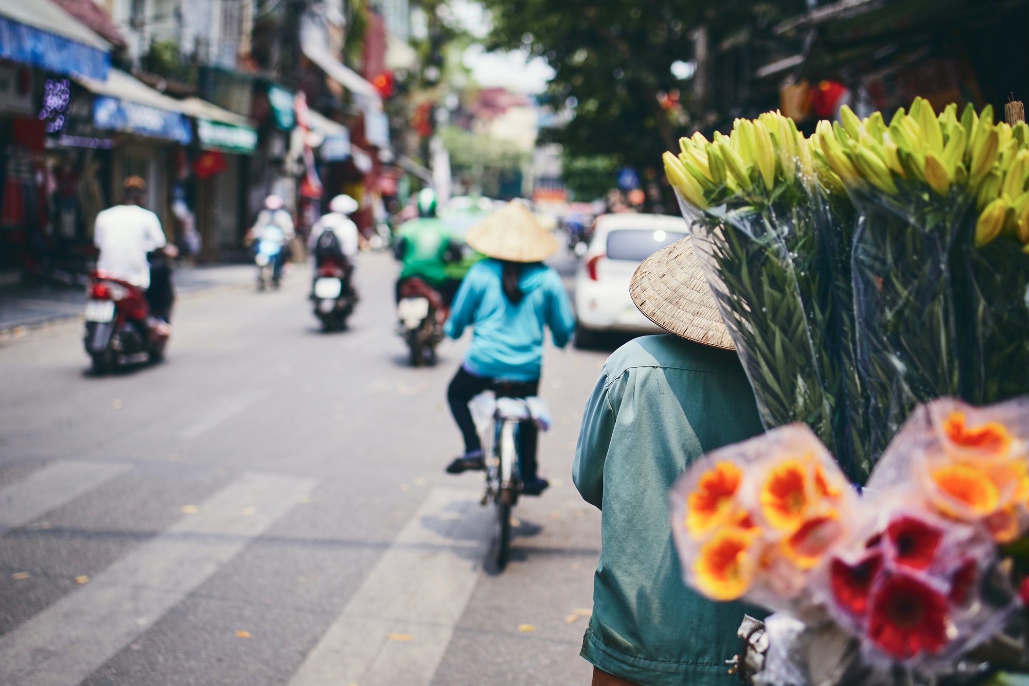 City life in street of old quarter in Hanoi. Flower vendor in traditional conical hat, Vietnam.